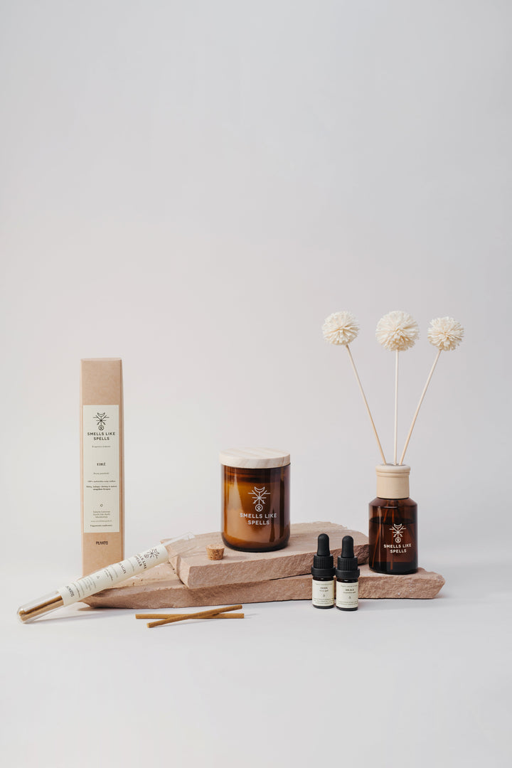 Amber glass home fragrance bottles, a scented candle, diffuser stems, incense and essential oils arranged on pale stone blocks.